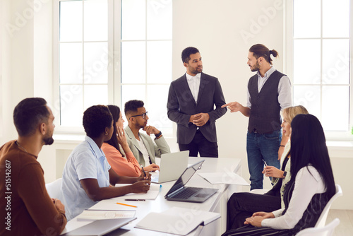 Mixed race group of serious employees sitting around office table during meeting in boardroom and listening to angry team manager criticizing marketing strategy or business project plan they prepared