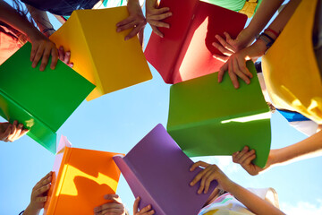 School children read books outdoors and learn about nature. Group of students standing in circle and holding red, green, yellow, orange and purple books in hands. Low angle bottom view shot from below