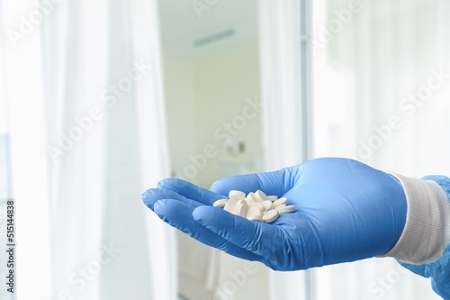 A medical worker or pharmacist hands wearing blue latex protective gloves  pouring white medicine pills