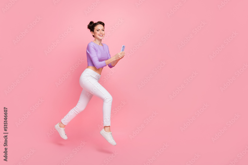 Full length body size view of lovely cheery trendy girl jumping using device copy space isolated over pink pastel color background Full length body size view of lovely cheery trendy girl jumping using device copy space isolated over pink pastel color background