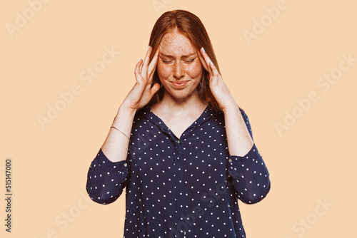 Canvas Print Upset stressed young redhead woman with freckle massaging temples feeling terrible headache migraine, sad tired sick caucasian girl isolated on beige studio background