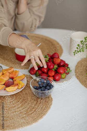 Obraz na płótnie The girl holds a krubnik in her hand and is going to eat it. A healthy fruit breakfast. Abundance of summer berries. Kubnik and blueberry w salonie