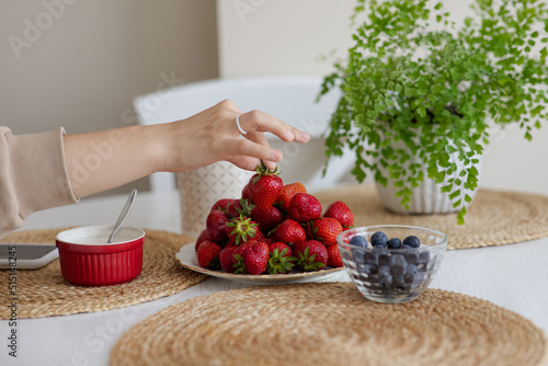 Obraz na płótnie The girl holds a krubnik in her hand and is going to eat it. A healthy fruit breakfast. Abundance of summer berries. Kubnik and blueberry w salonie