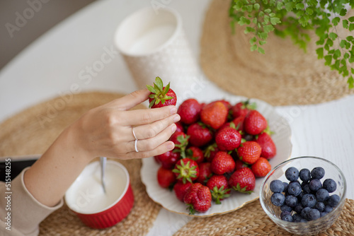 Obraz na płótnie The girl holds a krubnik in her hand and is going to eat it. A healthy fruit breakfast. Abundance of summer berries. Kubnik and blueberry w salonie