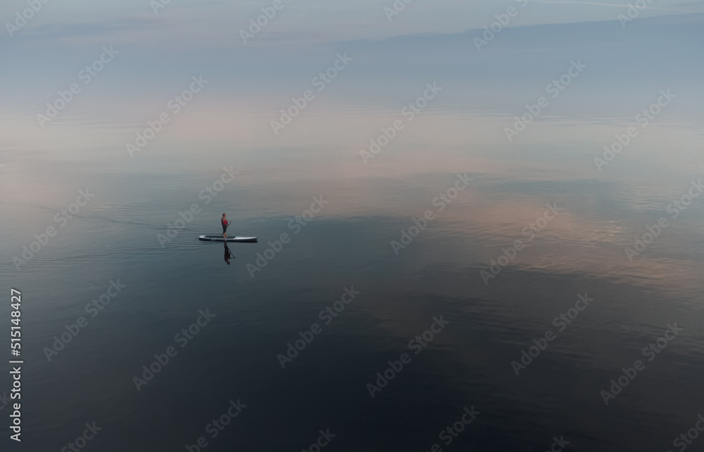 Fototapeta premium SUP surfer floats in an open calm sea. Aerial view