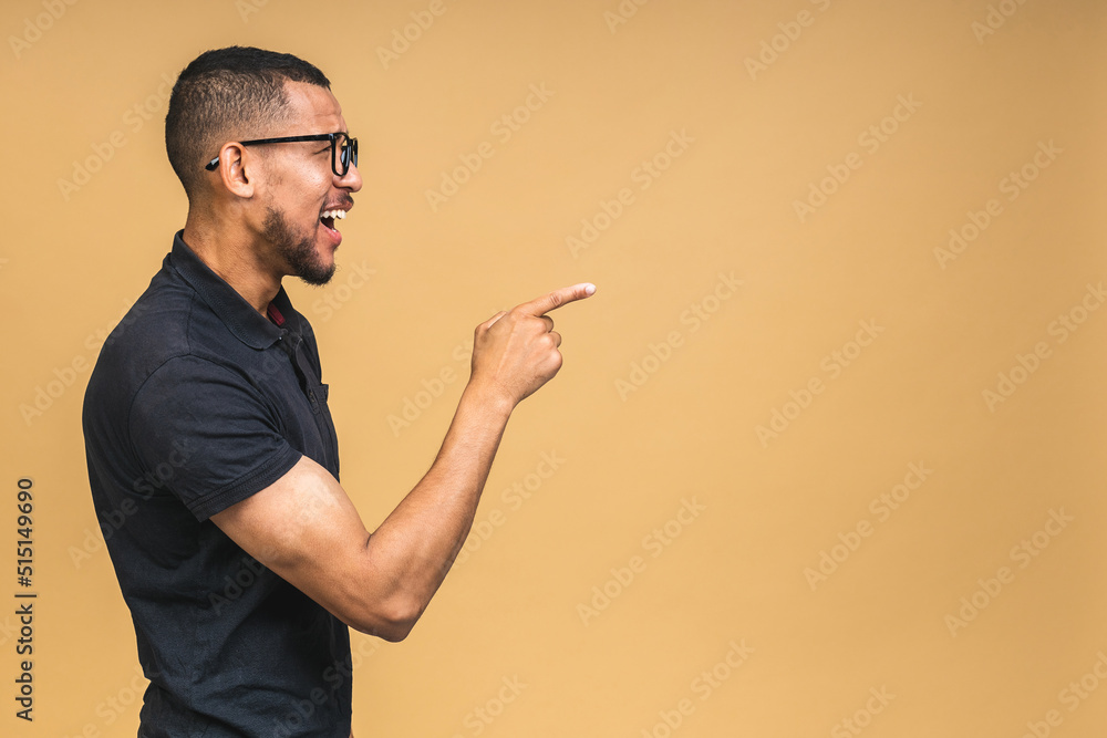 Portrait of happy young african american black man with in casual smiling, pointing aside with finger, isolated over beige background. Portrait of happy young african american black man with in casual smiling, pointing aside with finger, isolated over beige background.