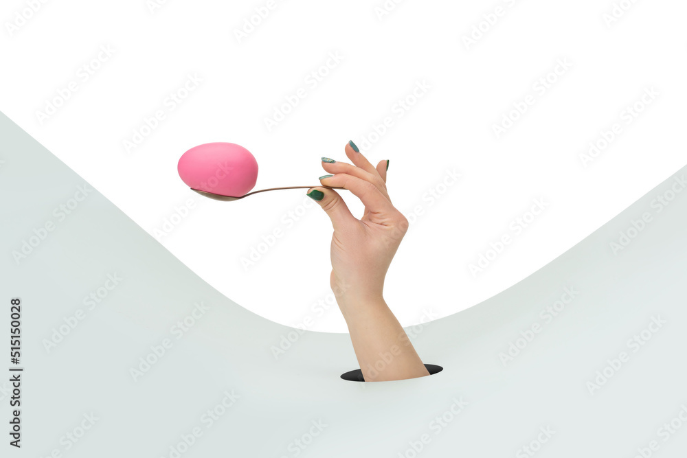 Female hand holding spoon with pink decorative easter egg on clean white and green background Female hand holding spoon with pink decorative easter egg on clean white and green background