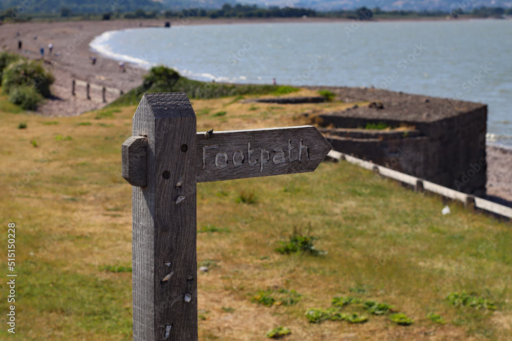 A public footpath sign stands in front of a sunny bay at Blue Anchor in Somerset. Looking west towards Minehead and Porlock