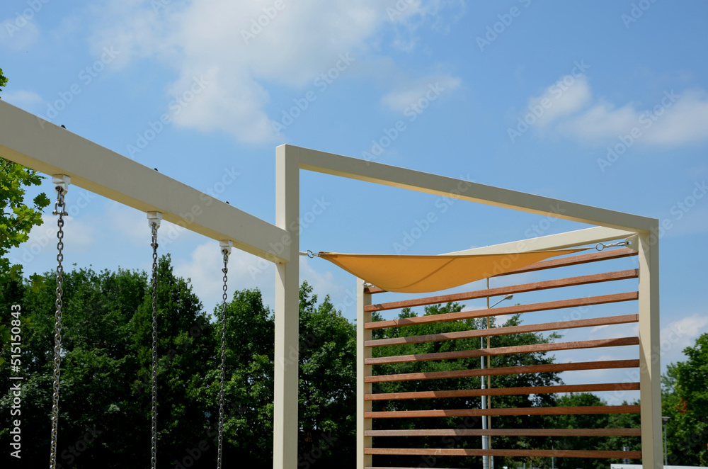 yellow canvas stretched, shading from the sun and rain over the terrace of the restaurant, on the playground in the kindergarten, on promenade. pergola with wooden gray beams, on white metal steel yellow canvas stretched, shading from the sun and rain over the terrace of the restaurant, on the playground in the kindergarten, on promenade. pergola with wooden gray beams, on white metal steel