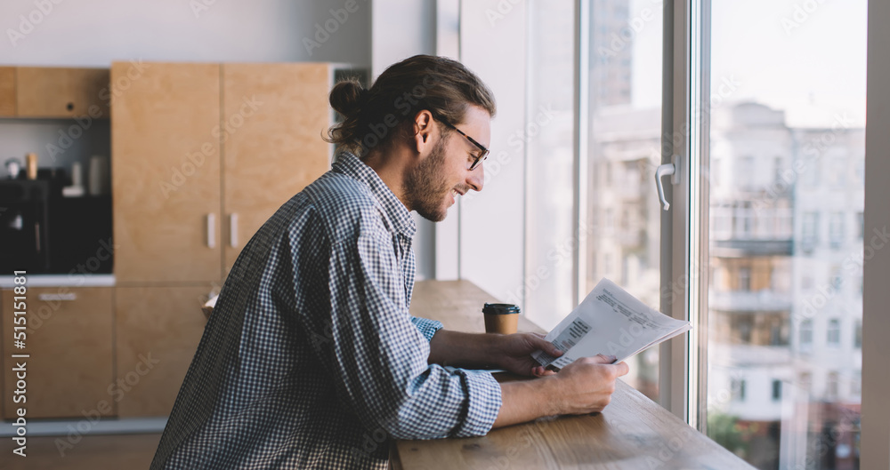 Side view of smart male student in classic eyeglasses analyzing informative notes while doing school homework, Caucasian hipster guy in spectacles and casual wear checking education test