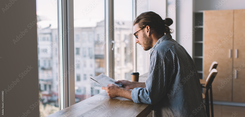 Millennial with newspaper at windowsill in office
