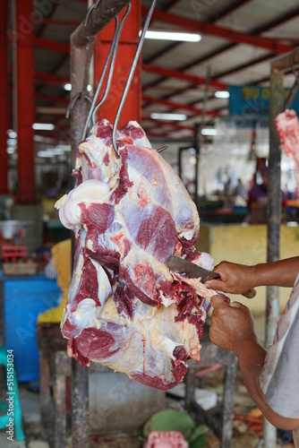 Butcher cut the meat working at indonesian Traditional market , cow carcassed on a hook. 