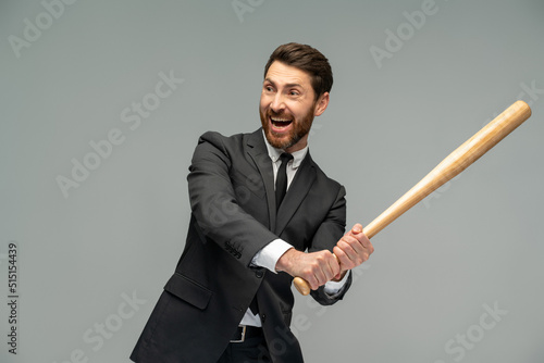 Waist up portrait view of the caucasian businessman swings with a baseball bat standing over grey background. Occupation concept