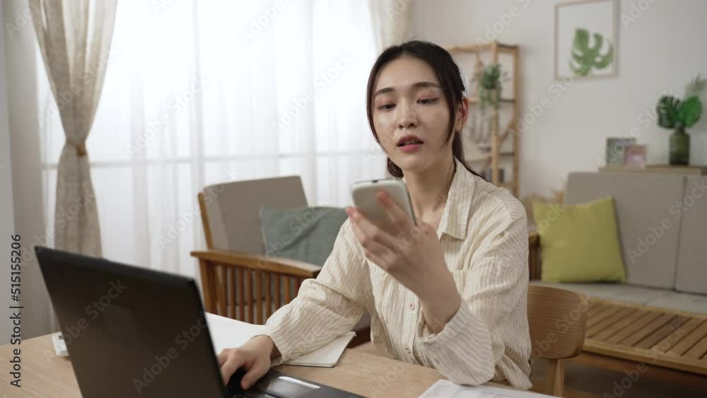 asian female manager breaking into smiles after getting a call from a friend on mobile phone while working from home with laptop in the living room. asian female manager breaking into smiles after getting a call from a friend on mobile phone while working from home with laptop in the living room.