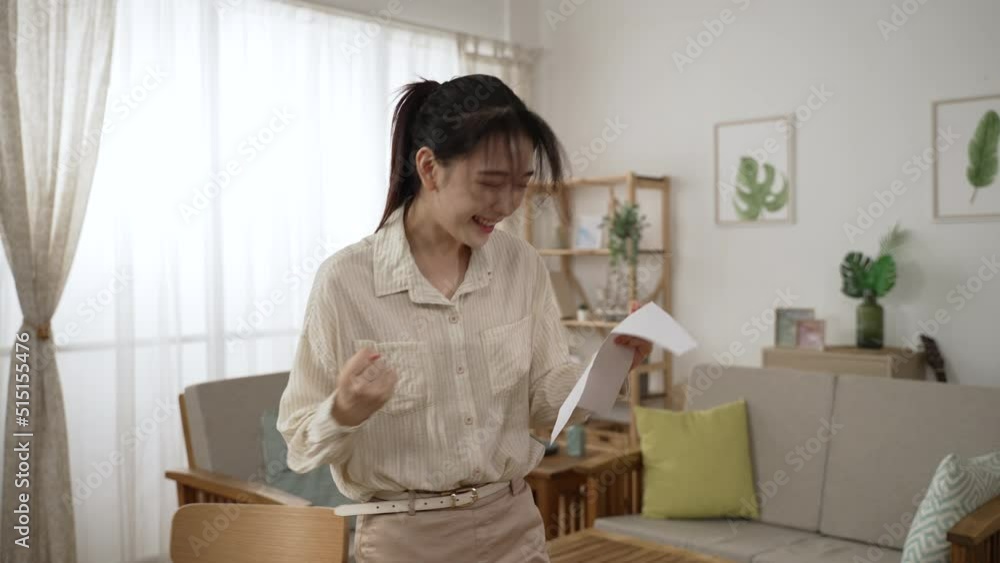 happy taiwanese female entrepreneur entering living room reading notification letter is screaming with joy while cheering for getting bank loan approval at home happy taiwanese female entrepreneur entering living room reading notification letter is screaming with joy while cheering for getting bank loan approval at home