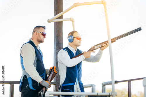 Two adult mans in sunglasses and a rifle vest practicing fire weapon shooting. Two young experienced shooters aiming shotgun in outdoor.