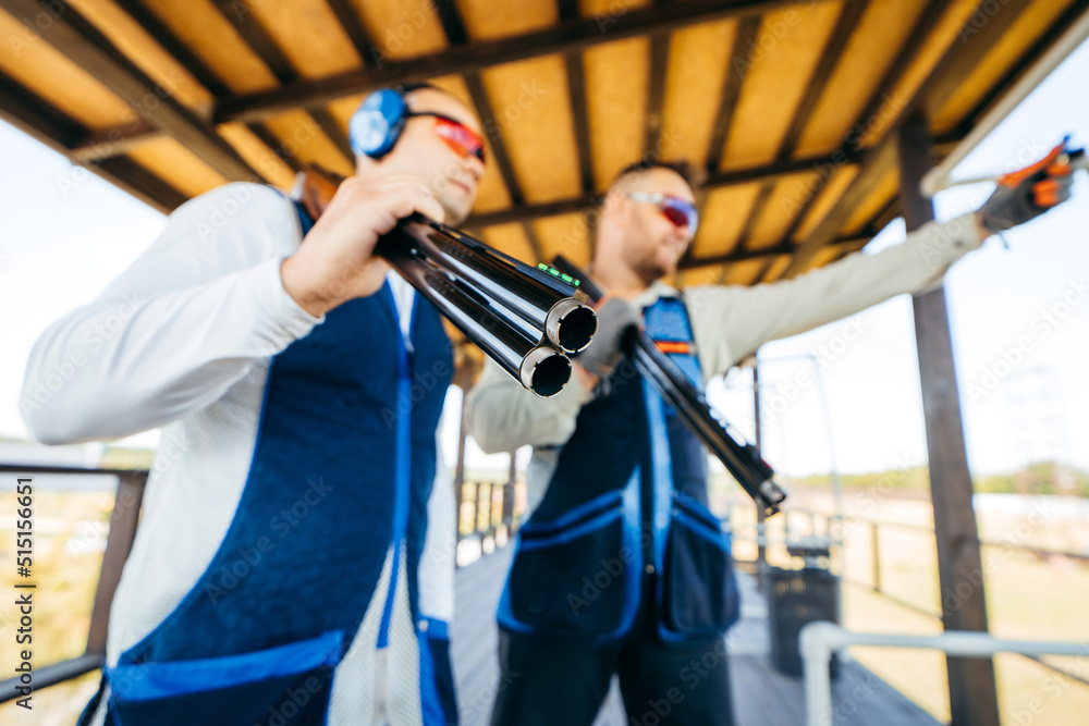 Φωτογραφία Blurred background of portraits of two adult mans in sunglasses, protective headphones and a rifle vest practicing fire weapon shooting