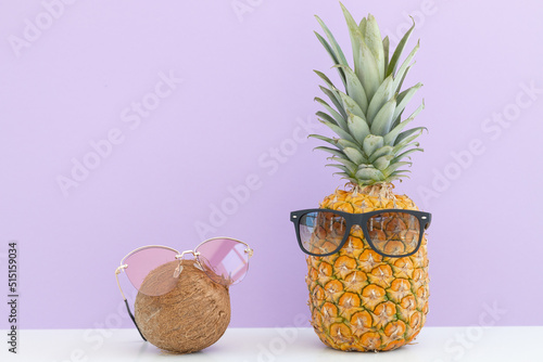 incised pineapple and coconut with sunglasses near a glass of juice and a cocktail straw