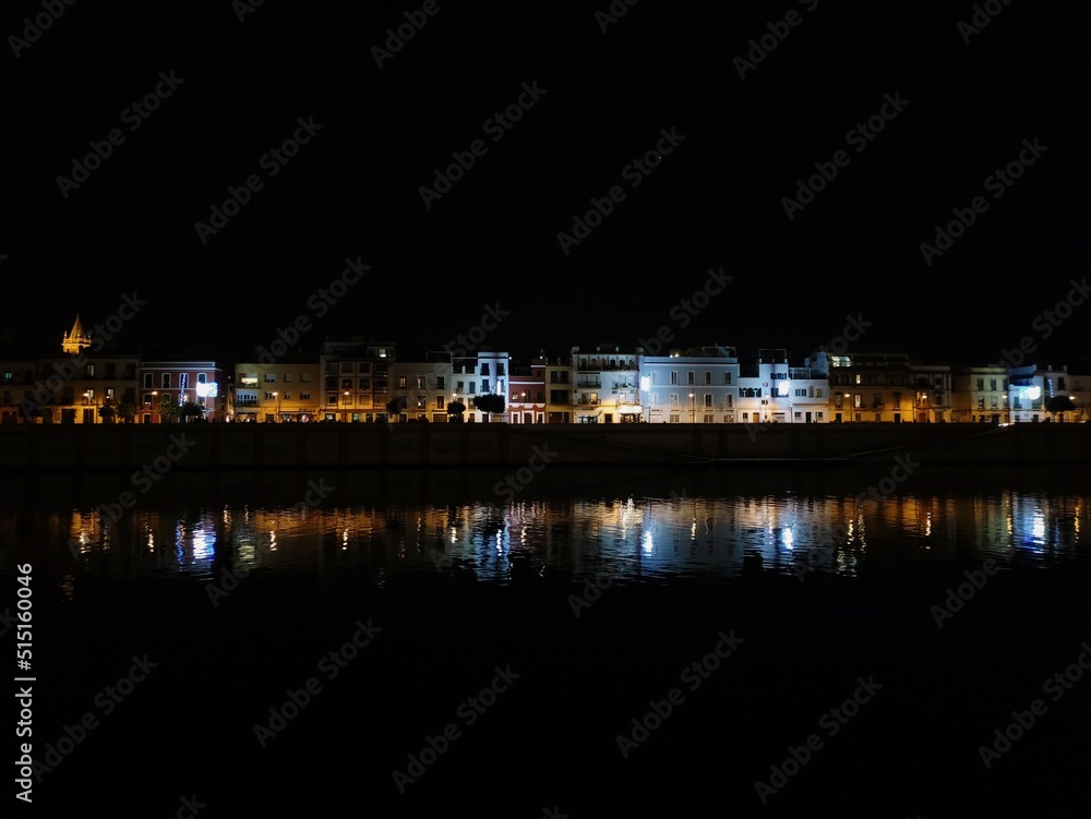 View of the city of Seville at night. With the Guadalquivir river in the foreground and the Triana bridge and Seville buildings in the background. nightlife concept. europe travel and ancient architec
