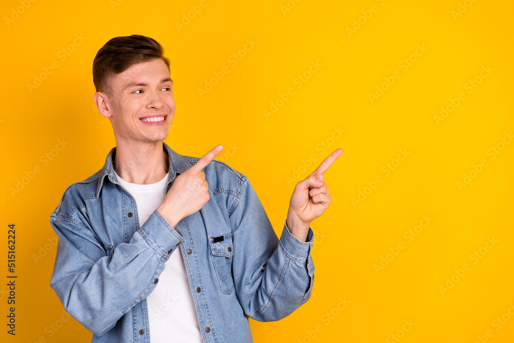 Photo of young cheerful guy indicate fingers empty space promotion banner isolated over yellow color background Photo of young cheerful guy indicate fingers empty space promotion banner isolated over yellow color background