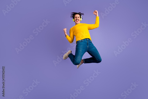 Full body of energetic overjoyed guy jumping raise fists shout yes rejoice isolated on purple color background