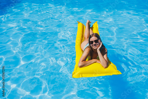 Pretty young woman in swimsuit and sunglasses lying on yellow inflatable mattresses in the pool. Enjoy sunbathing and relaxation.