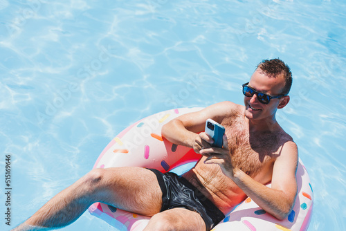 An attractive man is relaxing on an inflatable ring in the pool. A man in the pool is talking on the phone. vacation and free time concept