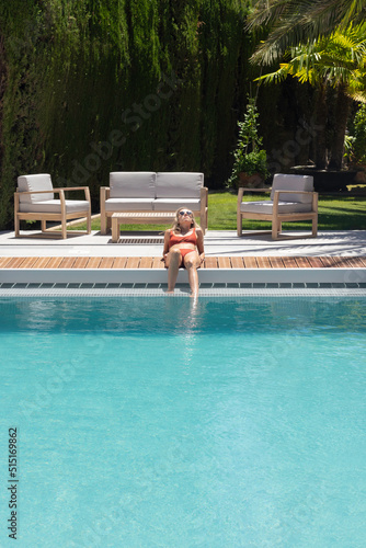 Vertical view of young woman laying in the edge of the swimming pool sun bathing to get tanned in summer