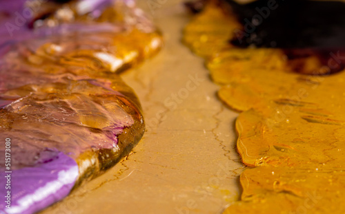 Purple yellow caramel mass for preparation of lollipops spread on pastry table. Cooking sweet candy. Handmade sweets. Background of sweet food, candies for holiday, childrens birthday. Extra close up.