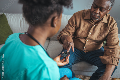 Happy senior man having his blood sugar measured in a nursing home by his caregiver. Happy nurse measuring blood sugar of a senior man in living room - diabetes and glicemia concept photo