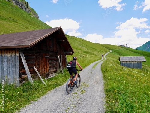 Mountain biking on gravel path in the Austrian Alps, ancient Walser town Buerstegg in the background. Lech, Arlberg, Austria.