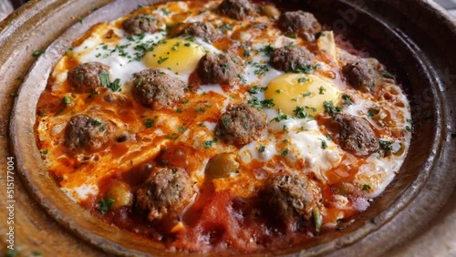 A  traditional kefta (kofta) meal served in a tajine, tagine in a Moroccan clay pot, hot, and sizzling. Traditional Moroccan slow-cooked meal with meatballs (meatloaf) and eggs. 4k. photo