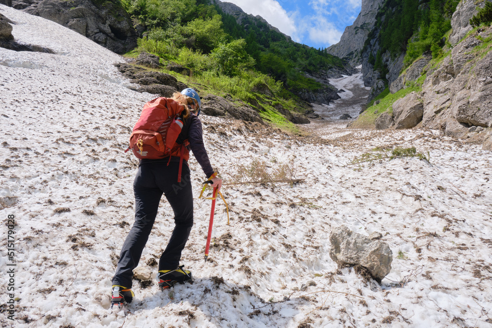 Woman alpinist with ice axe, crampons and backpack, hikes up on late Summer snow in the White Valley, an unmarked alpine route in Bucegi mountains, Romania.
