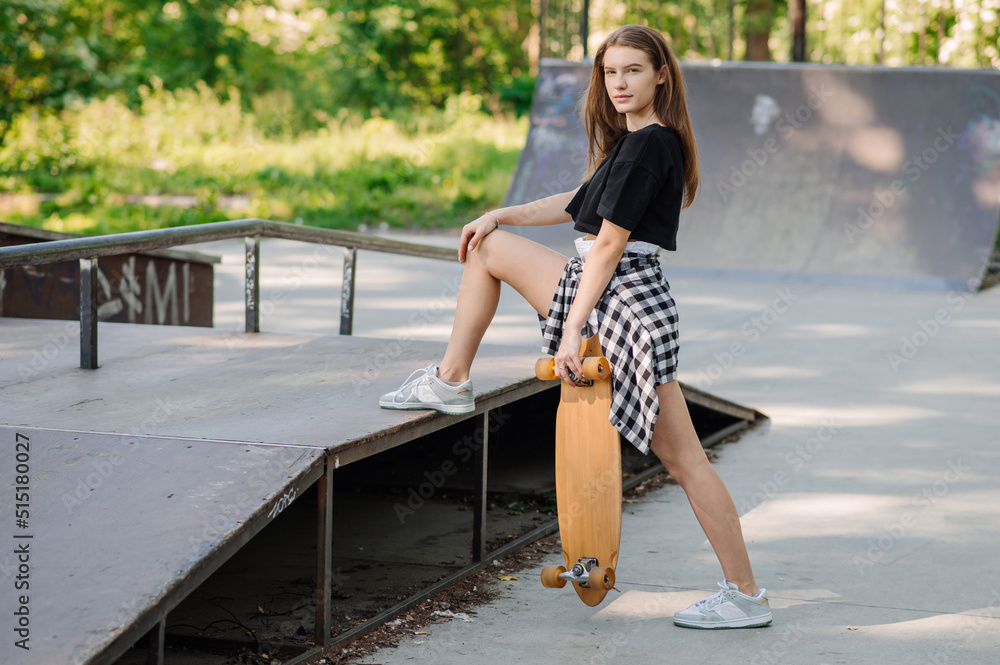 Female teenager with a skateboard walking on the ramp in the skate park