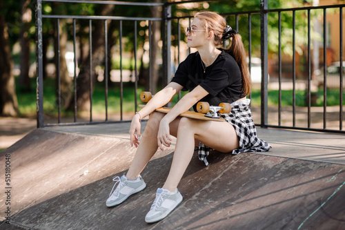 Teenager skater girl is sitting and resting on the ramp in the skate park