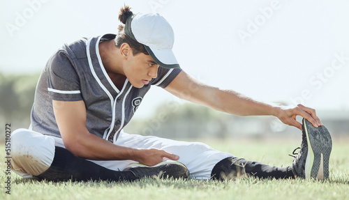 Full length of a baseball player sitting on a pitch and stretching before playing a game. Serious and focused athlete getting ready to play match on grass. Fit, active, sporty, athletic man