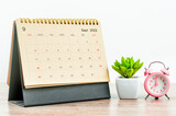 The September 2022 green Desk calendar with pink alarm clock on wooden table.
