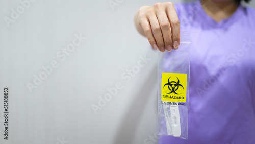 Plastic bag with biohazard symbol using to contain ATK test kit for separation disposal, holding by human hand. Healthcare and medical object. Close-up and selective focus with copy space.