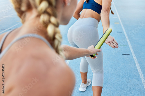 Relay race athlete handing the baton over to a teammate while running from behind. Rearview closeup of two female athletes working together as a team to compete in and win a sports competition