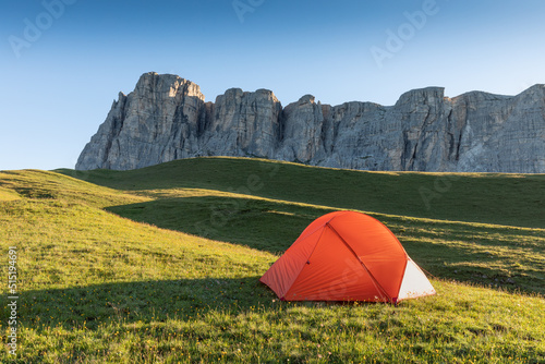 A glowing tent in the mountains under a blue morningsky. Sunrise and mountains in the background. Summer landscape. Panorama Bright tourist tent in the mountains nature.