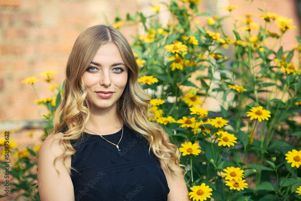 Young beautiful woman in a black dress enjoys the smell of blooming yellow flowers. Outdoor portrait in blooming spring park Young beautiful woman in a black dress enjoys the smell of blooming yellow flowers. Outdoor portrait in blooming spring park