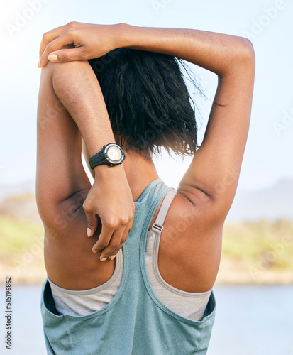 Fotografie One active woman from the back stretching arms and triceps by pulling elbow towards spine while exercising outdoors