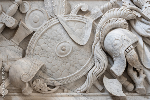 Close-up on ancient roman shield, weapons and helmets carved in a decorated marble wall © Giorgio G