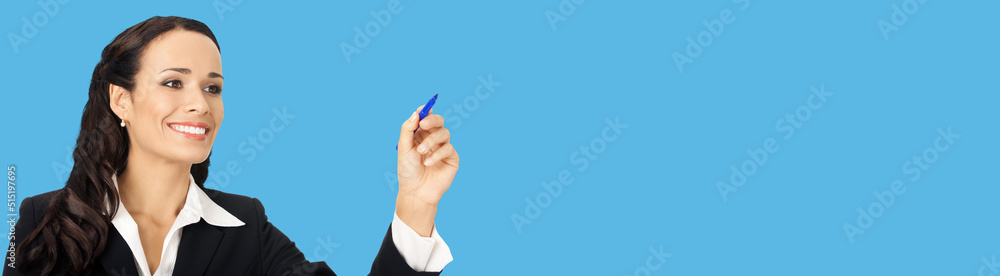 Portrait of happy smiling beautiful young businesswoman in black confident suit, writing or drawing something on screen, by marker. Brunette woman, isolated on blue background Portrait of happy smiling beautiful young businesswoman in black confident suit, writing or drawing something on screen, by marker. Brunette woman, isolated on blue background