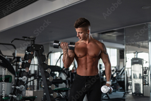 Muscular athletic handsome guy with athletic body hair working out and doing exercises with dumbbells in the gym