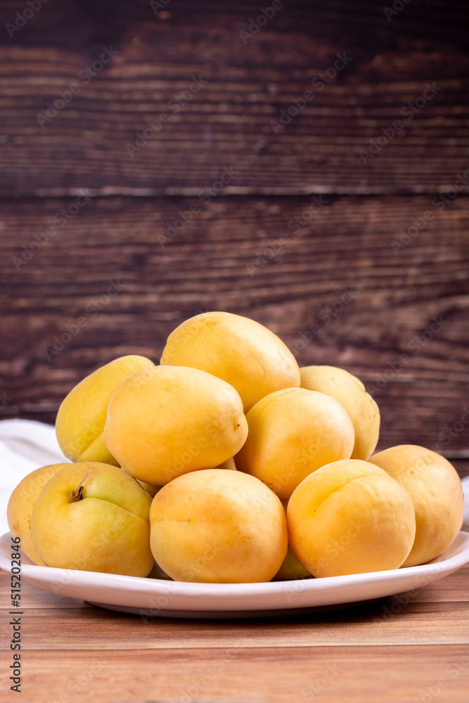 Apricots on wood background. Pile of fresh apricots in a white plate. close up Apricots on wood background. Pile of fresh apricots in a white plate. close up