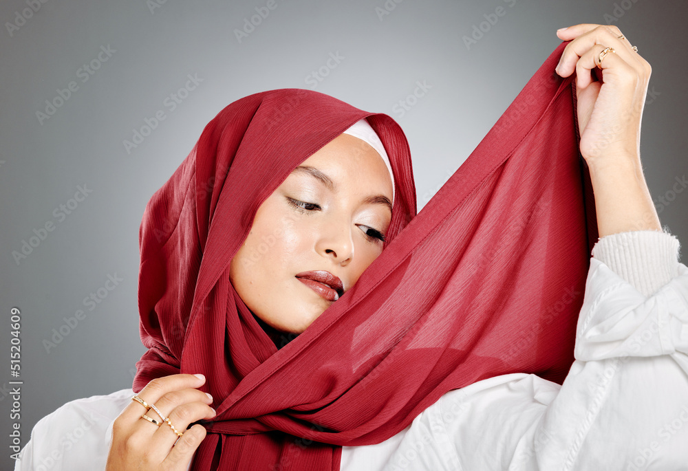 A classy muslim woman wearing a red hijab or headscarf isolated against grey background with copyspace. Confident female wrapping her head in a traditional scarf while getting dressed in a studio A classy muslim woman wearing a red hijab or headscarf isolated against grey background with copyspace. Confident female wrapping her head in a traditional scarf while getting dressed in a studio