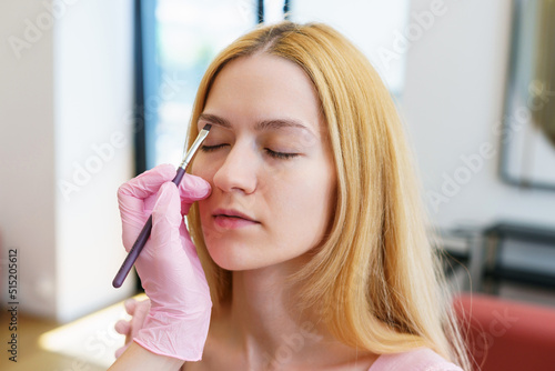Close-up of the process of creating the correct shape of the eyebrows. A young woman in a beauty salon with an eyebrow master