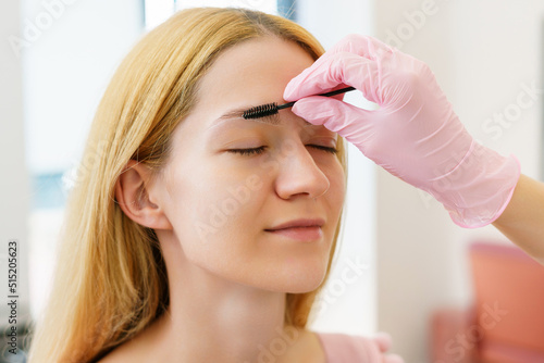 Close-up of the face of a young woman whose eyebrow master combs the hairs on her eyebrows with a black brush