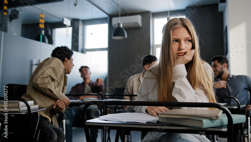 Sad frustrated insecure girl student sitting in classroom at desk suffering from abuse bad attitude ridicule from classmates young woman feeling humiliated distressed lonely concept discrimination